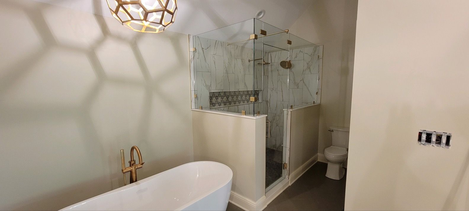 A modern bathroom featuring a white soaking tub, a glass-enclosed shower, a toilet, and a geometric pendant light. A modern bathroom featuring a white soaking tub, a glass-enclosed shower, a toilet, and a geometric pendant light.