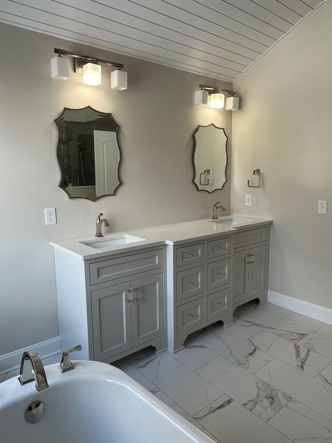 Modern double bathroom vanity with gray cabinets, white marble countertops, two mirrors, and overhead light fixtures. Modern double bathroom vanity with gray cabinets, white marble countertops, two mirrors, and overhead light fixtures.