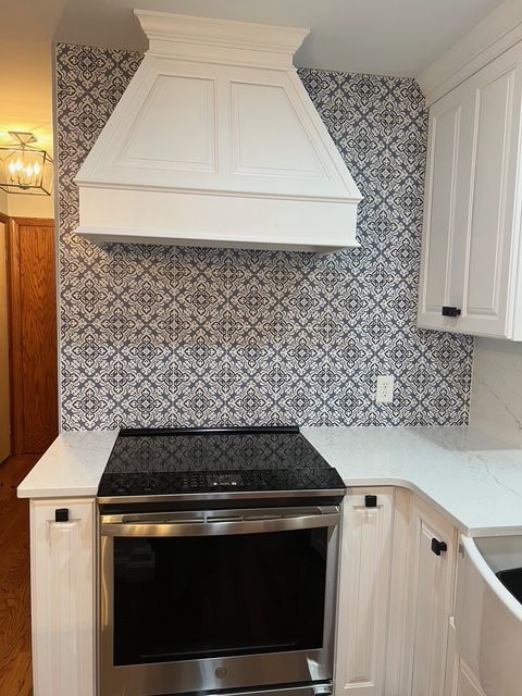 A modern kitchen stove with a white range hood set against a black-and-white patterned tile backsplash.