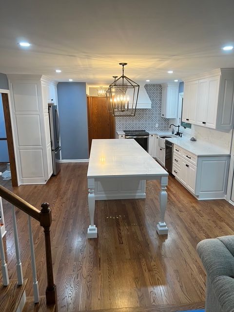 A bright, modern kitchen with white cabinets, a large central island, stainless appliances, and polished hardwood floors. A bright, modern kitchen with white cabinets, a large central island, stainless appliances, and polished hardwood floors.
