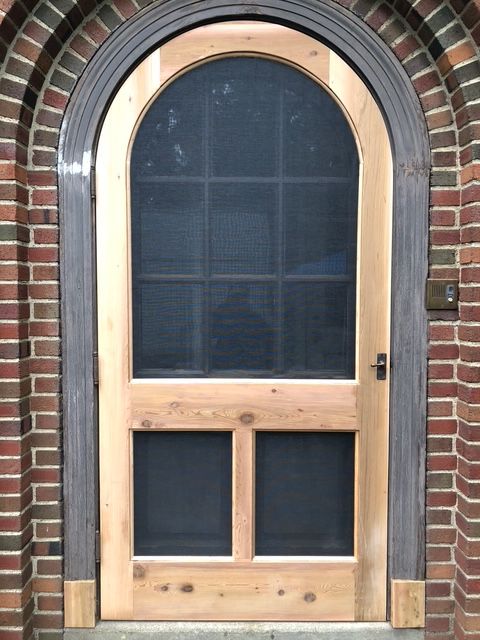 An arched wooden screen door installed in a brick doorway.