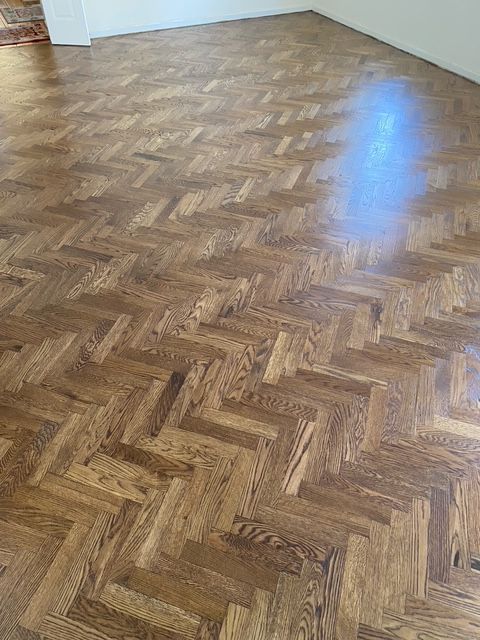 Brown hardwood flooring laid in a herringbone pattern with a polished, reflective finish.