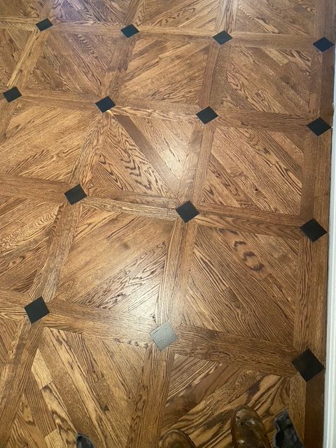 Hardwood floor with a diagonal basketweave pattern featuring light brown wood planks and small, dark square corner inlays. Hardwood floor with a diagonal basketweave pattern featuring light brown wood planks and small, dark square corner inlays.