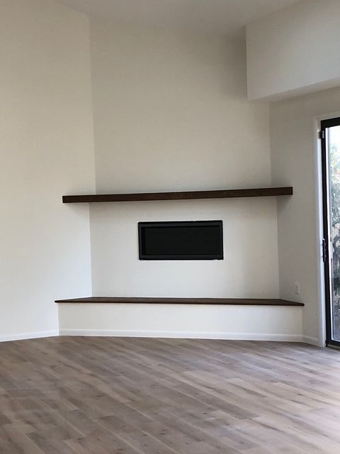 A modern room with wood floors features a corner fireplace with a black insert between two dark wood shelves.