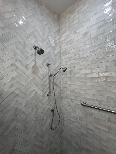 A shower stall with light, glossy tiles in herringbone and brick patterns, featuring a dual shower head system and grab bar.