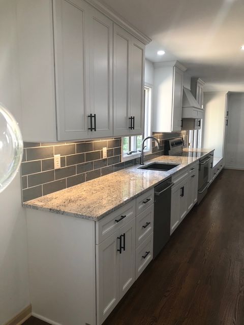 Modern kitchen with white cabinets, speckled granite countertops, a grey subway tile backsplash, and dark wood flooring. Modern kitchen with white cabinets, speckled granite countertops, a grey subway tile backsplash, and dark wood flooring.