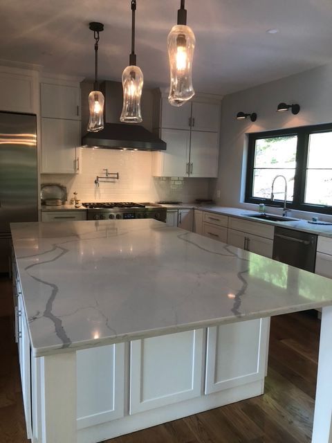 Modern white kitchen with a large marble-topped island, three glass pendant lights, and dark framed windows. Modern white kitchen with a large marble-topped island, three glass pendant lights, and dark framed windows.