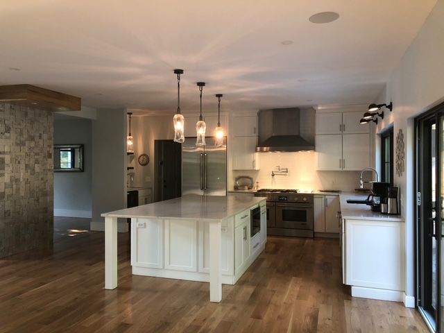 Modern kitchen with a white central island, stainless steel appliances, pendant lighting, and hardwood floors. Modern kitchen with a white central island, stainless steel appliances, pendant lighting, and hardwood floors.