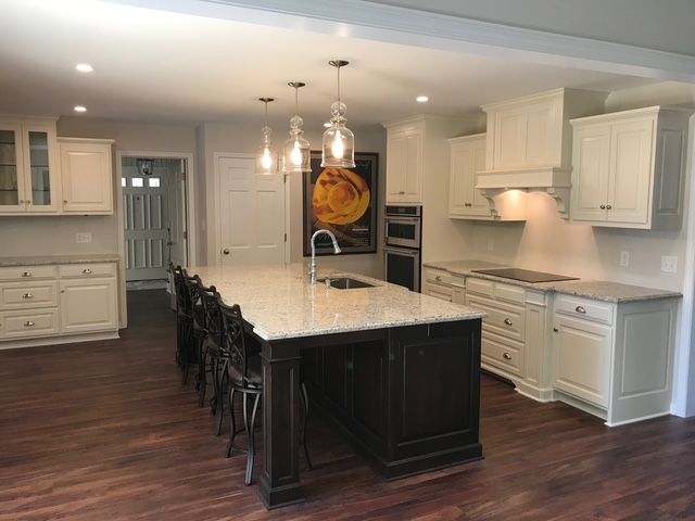 A modern kitchen features a dark island with stone countertops, white cabinetry, and three pendant lights over a wood floor. A modern kitchen features a dark island with stone countertops, white cabinetry, and three pendant lights over a wood floor.