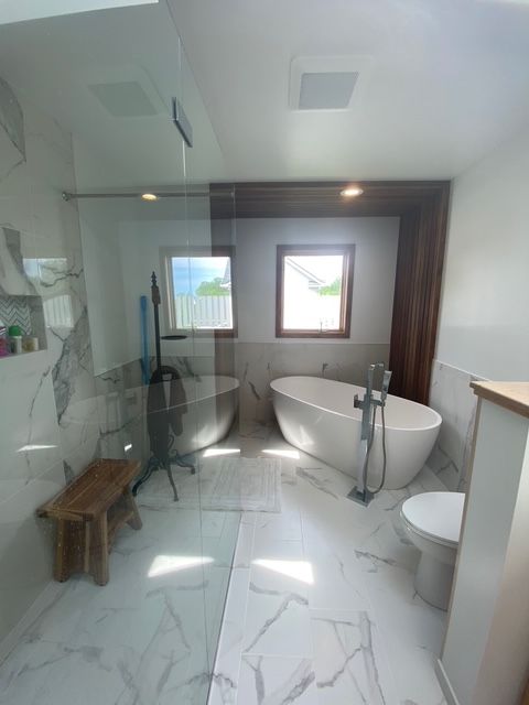A modern bathroom featuring a white freestanding tub, a glass-enclosed shower, a wooden bench, and marble-patterned flooring. A modern bathroom featuring a white freestanding tub, a glass-enclosed shower, a wooden bench, and marble-patterned flooring.