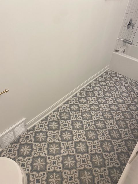 A bathroom with white walls and a tub, featuring patterned gray and white tile flooring.