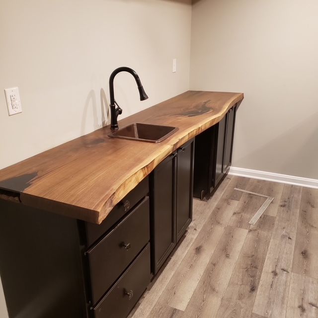 A wet bar with dark cabinets and a live-edge walnut wood countertop, featuring a small sink and modern dark faucet. A wet bar with dark cabinets and a live-edge walnut wood countertop, featuring a small sink and modern dark faucet.