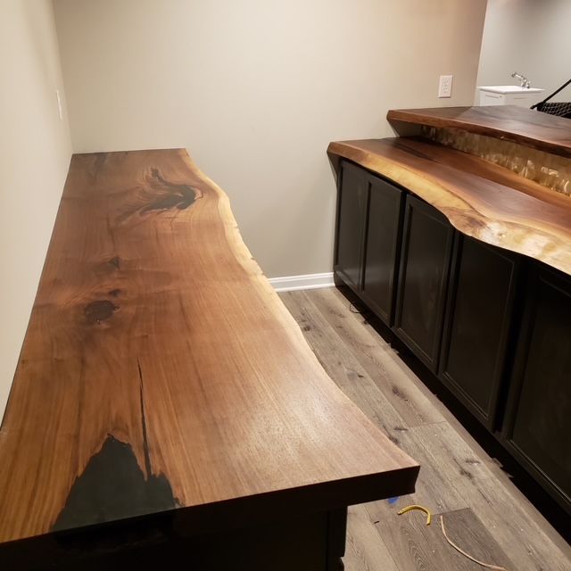 Live edge wood bar countertops with dark cabinetry in a room with light wood-look flooring and light walls.