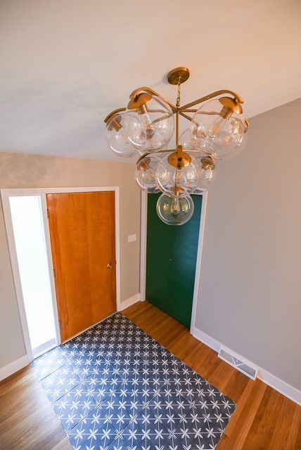 A high-angle view of a foyer with wood floors, a blue patterned rug, a wood door, a green door, and a globe chandelier.