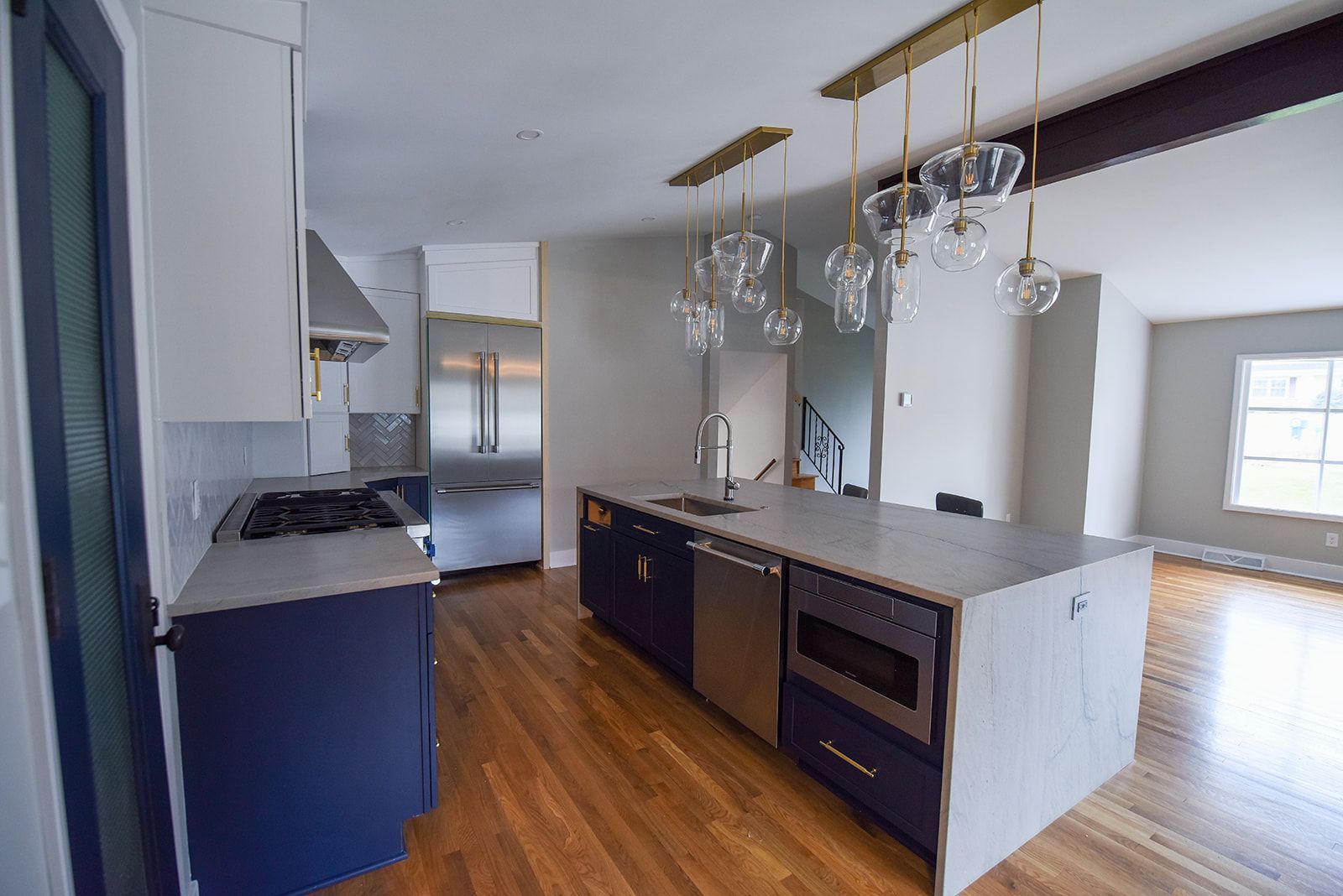 Modern kitchen with navy cabinets, a white stone island, stainless steel appliances, and hanging glass pendant lights.