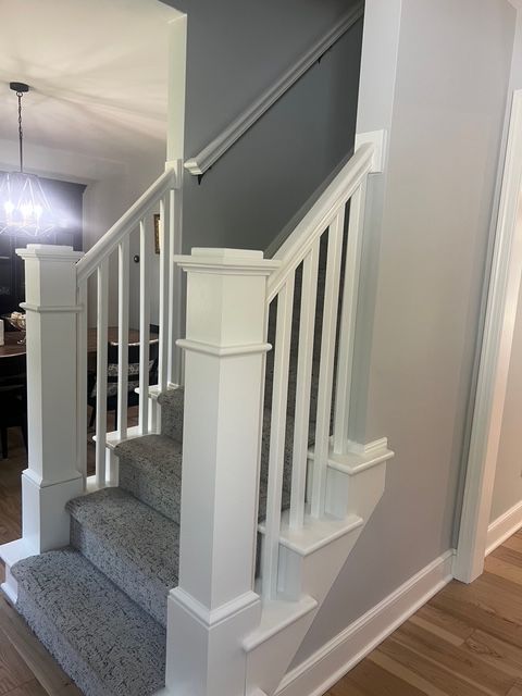 A staircase with gray carpet steps, white wood balusters and posts, and a dark gray accent wall in a bright home interior.