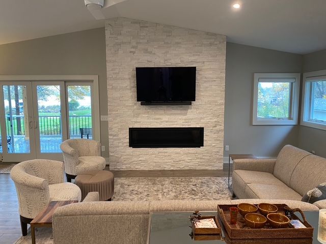 A modern living room features a white stone fireplace with a mounted television and a sleek, rectangular electric insert.