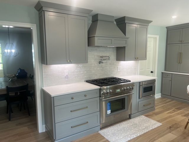 A modern kitchen with grey cabinetry, a stainless steel stove, and a marble-tiled backsplash under warm lighting. A modern kitchen with grey cabinetry, a stainless steel stove, and a marble-tiled backsplash under warm lighting.