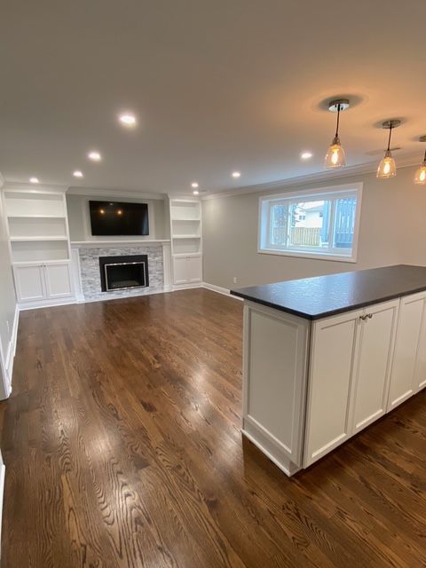 A wide-angle view of a modern open-concept living area with white built-in shelving, a fireplace, and a kitchen island.