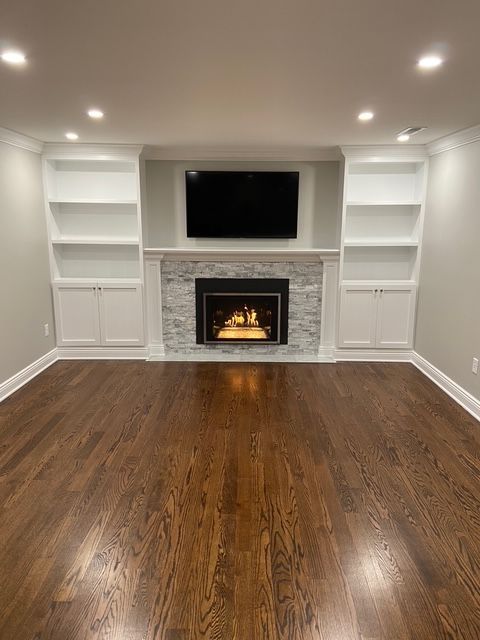 A room with dark wood floors, built-in white shelves flanking a stone fireplace with a mounted television.
