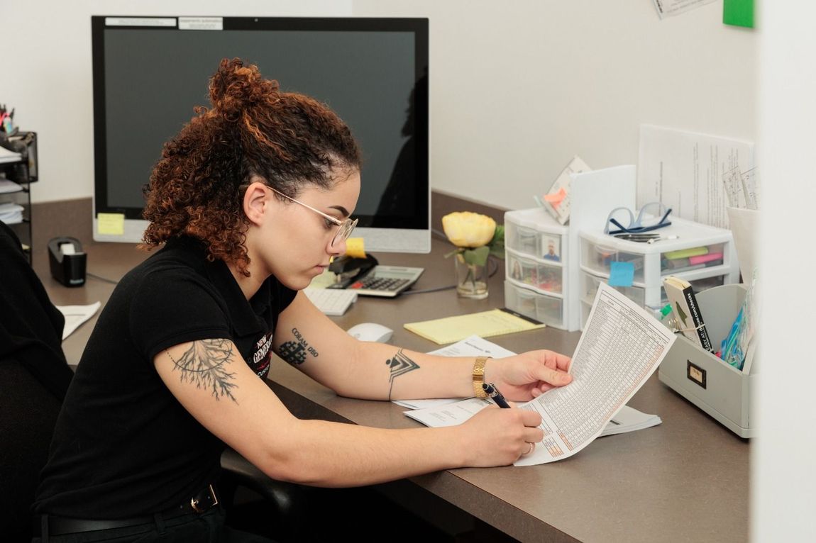 A woman is sitting at a desk looking at a piece of paper.