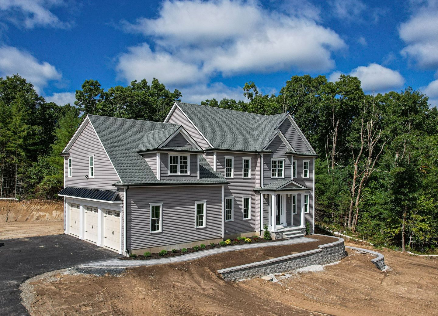 A large house is sitting on top of a dirt hill surrounded by trees.