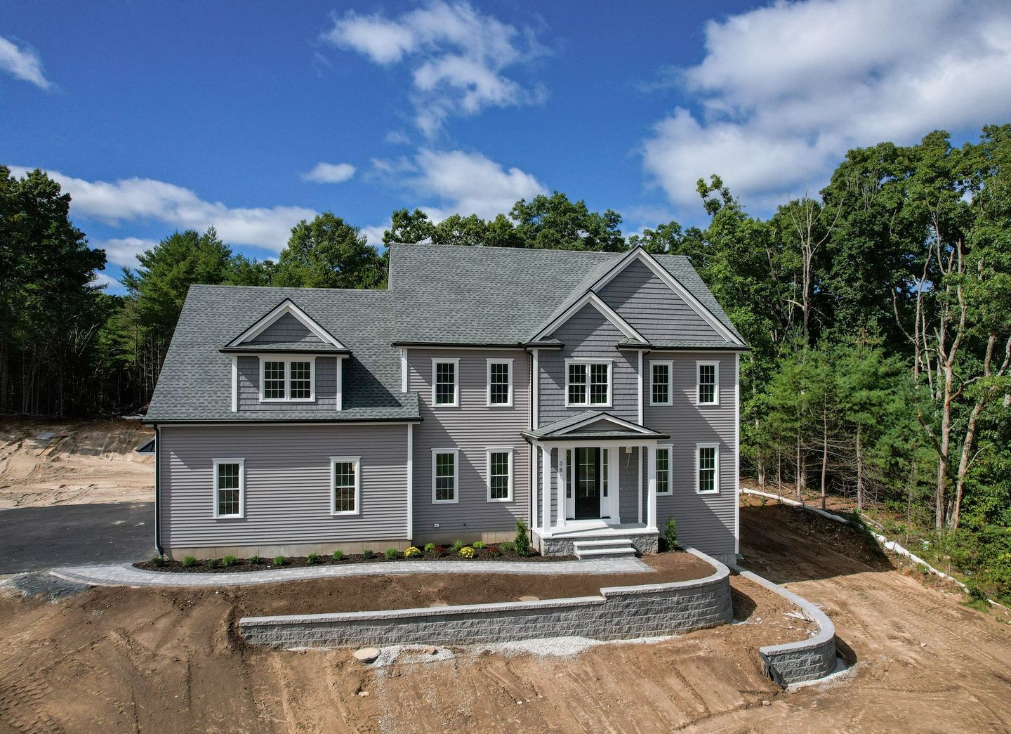 A large house is sitting on top of a dirt hill surrounded by trees.