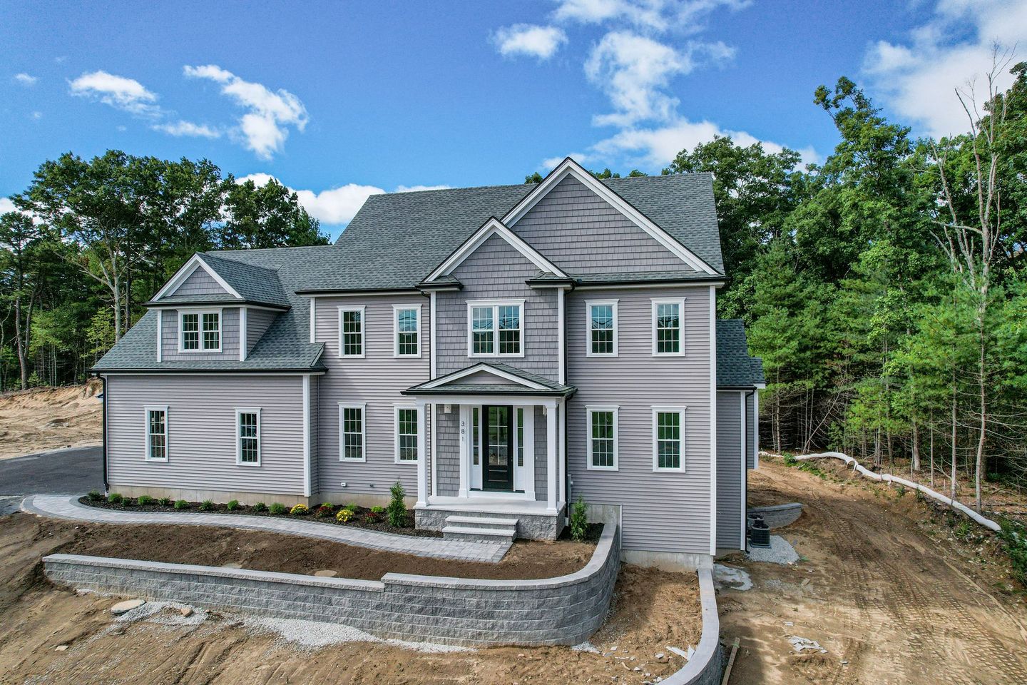 A large house is sitting on top of a dirt hill surrounded by trees.