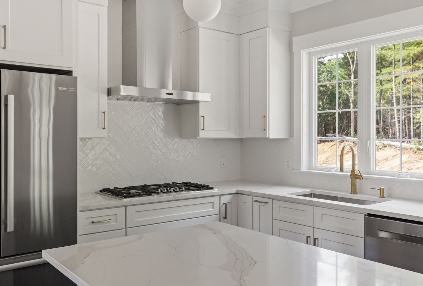 A kitchen with white cabinets , a stove top oven , a refrigerator , a sink , and a window.