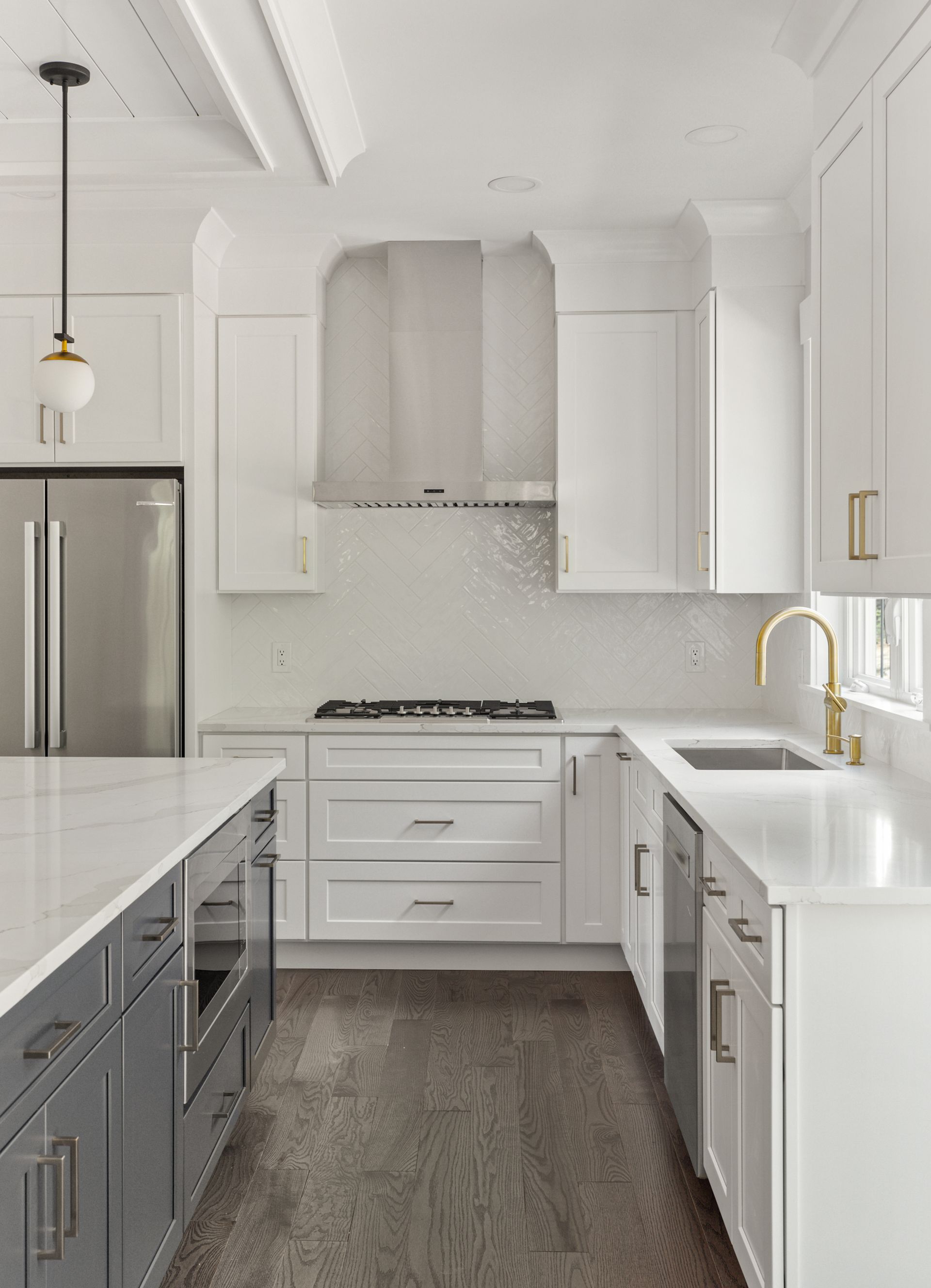 A kitchen with white cabinets , gray cabinets , stainless steel appliances and a large island.