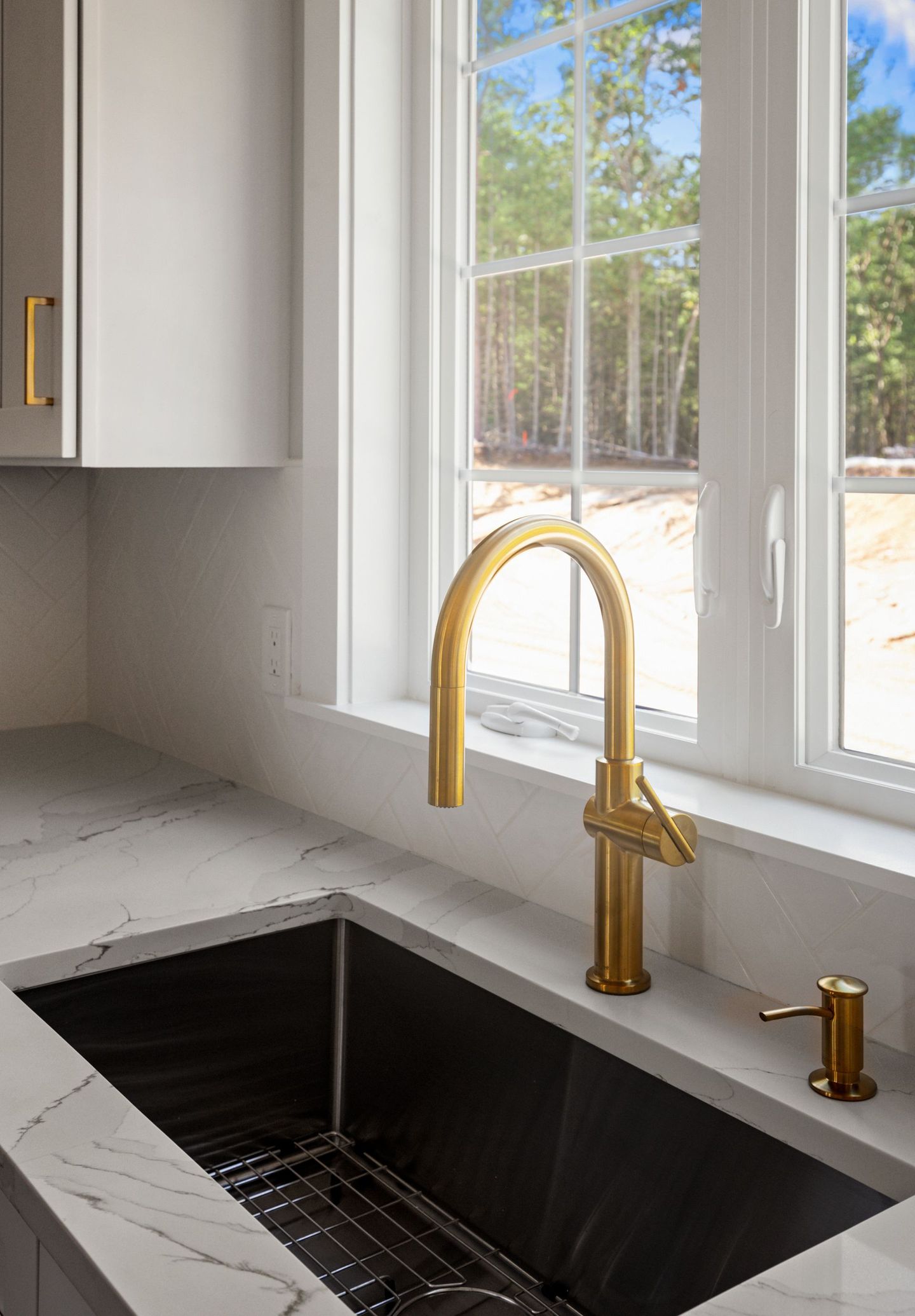 A kitchen sink with a gold faucet and a window.