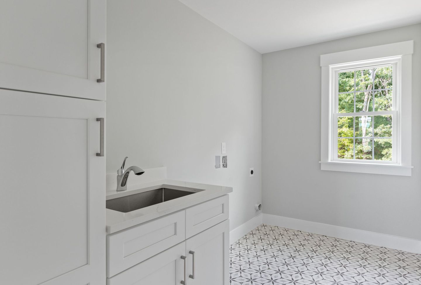 A laundry room with a sink , cabinets , and a window.