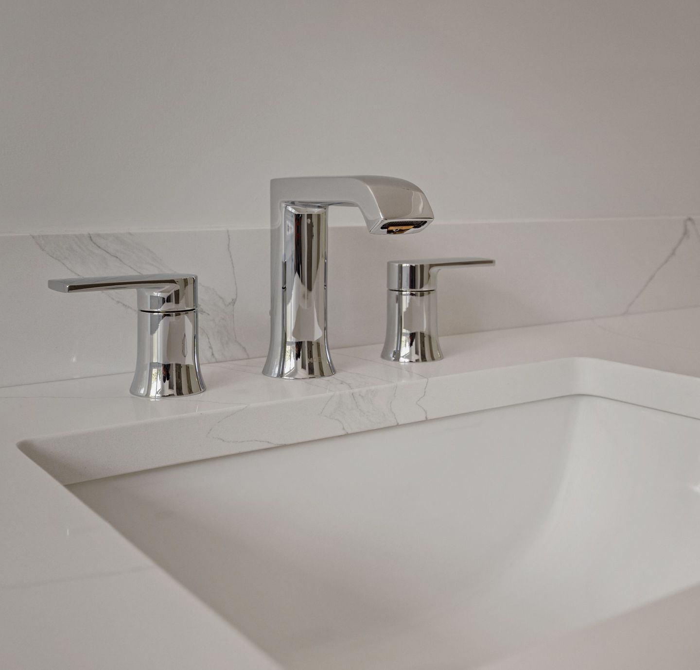 A bathroom sink with a chrome faucet and handles