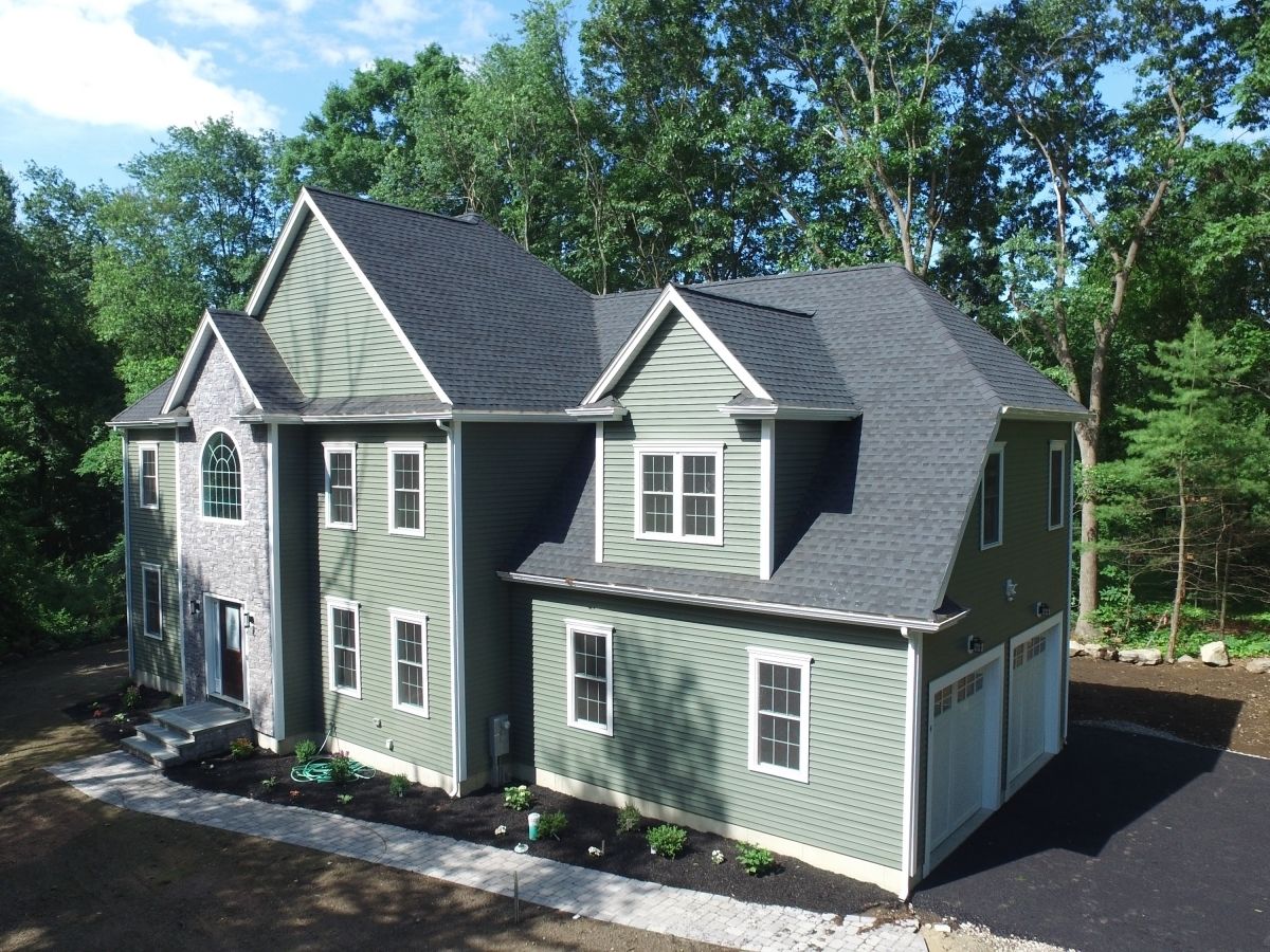 A large green house with a black roof is surrounded by trees.