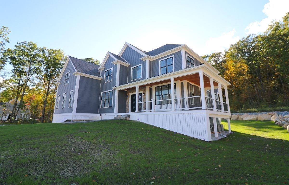 A large house with a large porch is sitting on top of a lush green hill.