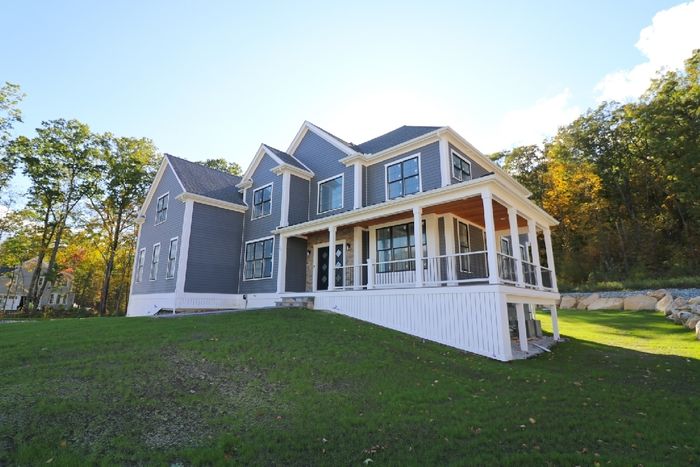 A large house with a large porch is sitting on top of a lush green hill.