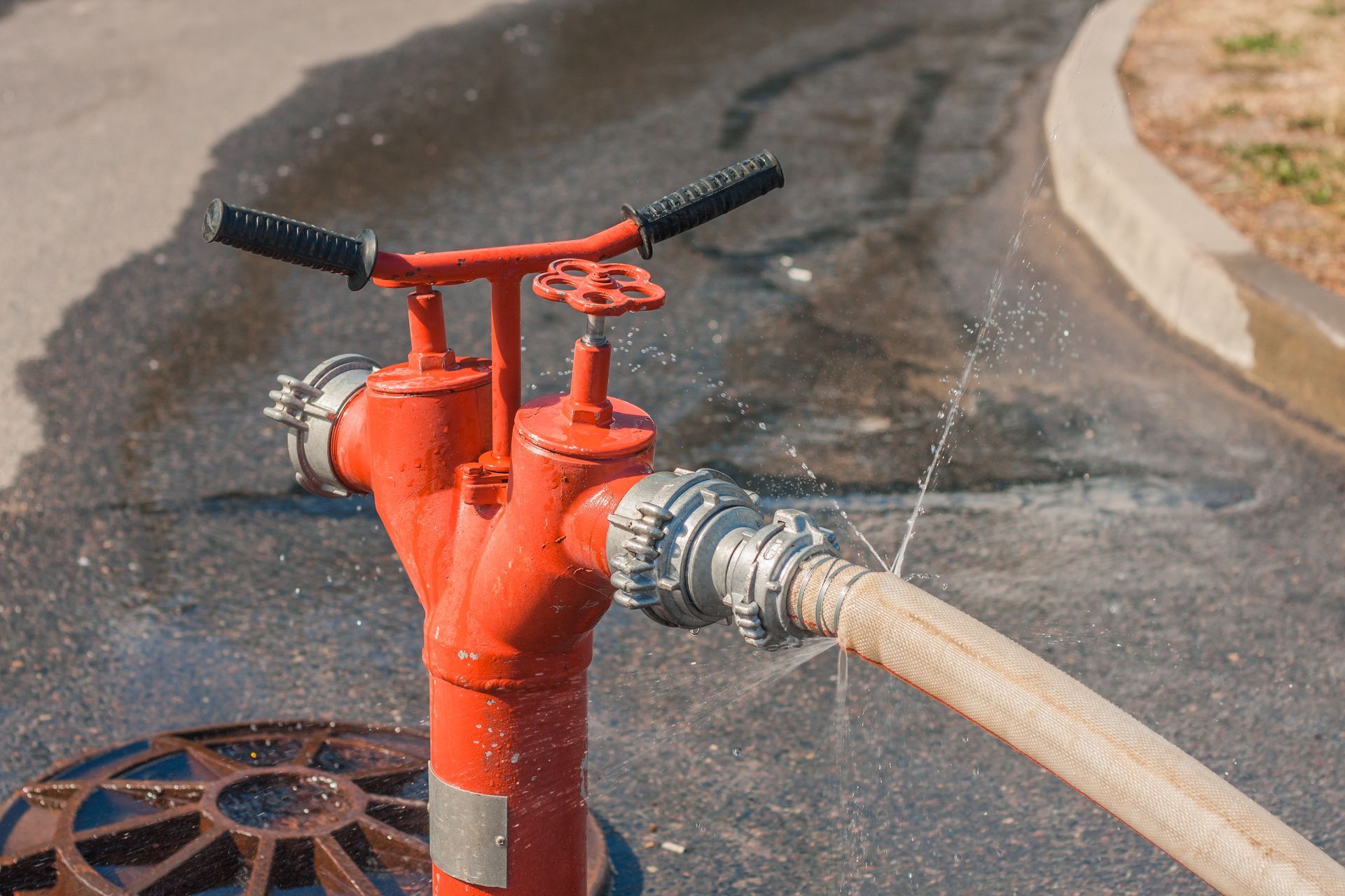 Water sprays from a damaged orange fire hose, with a floor with gravel on the background.
