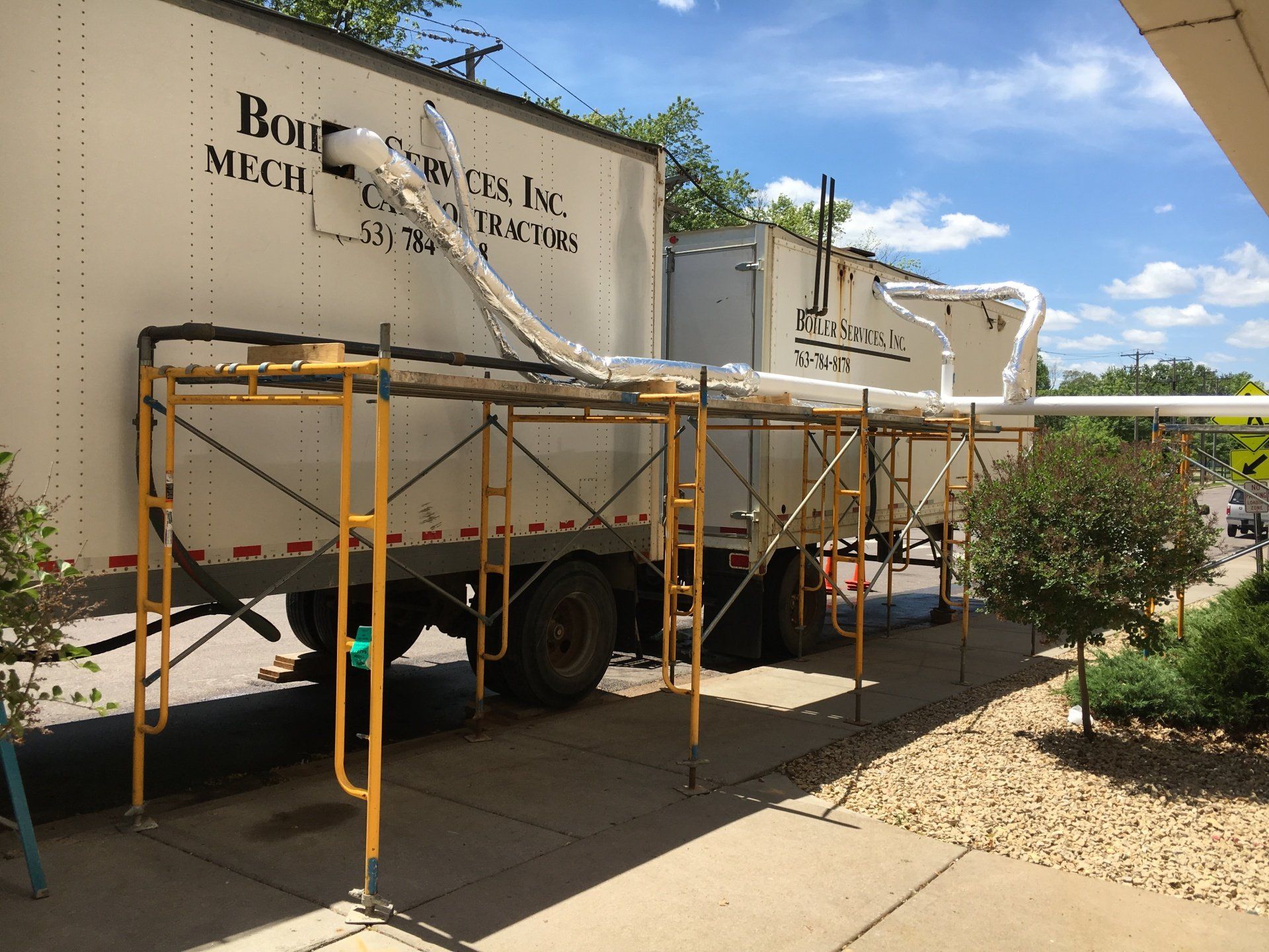 A white trailer on scaffolding with pipes and the words 