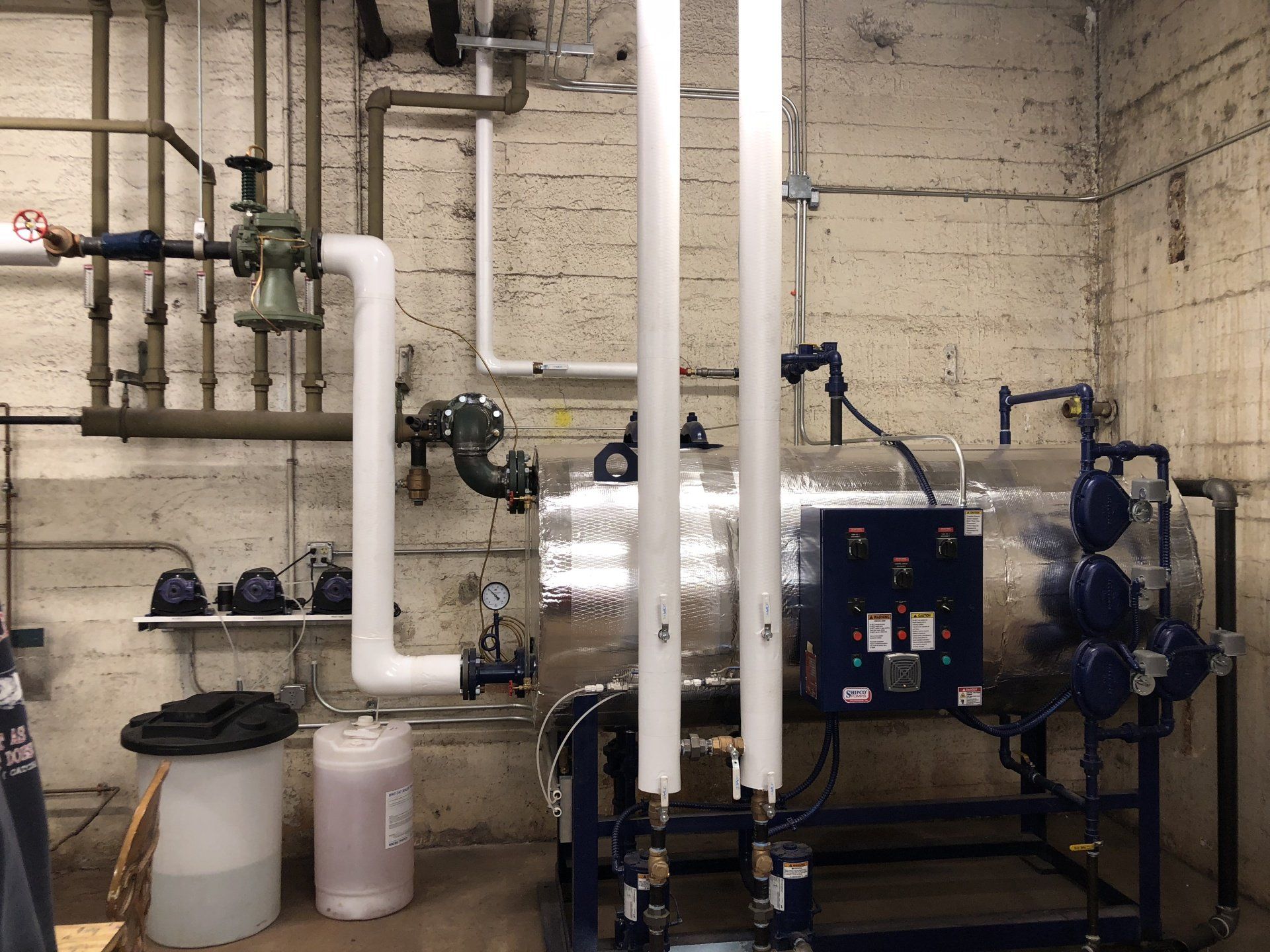 Industrial water heater system with insulated pipes and control panel in a utility room.