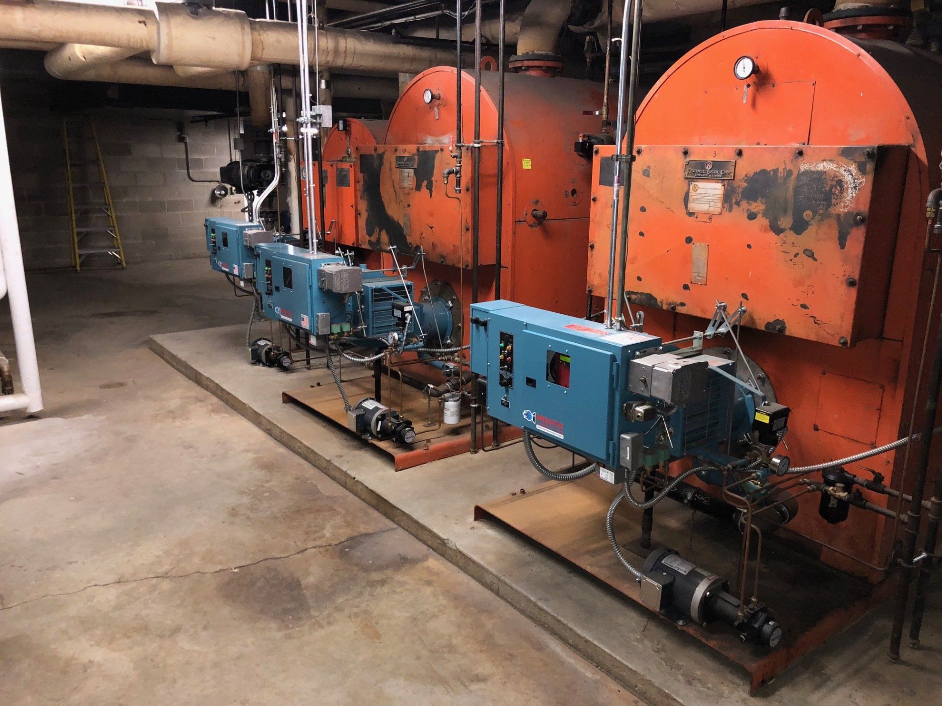 Industrial boiler room with orange boilers, blue burners, and pipes.