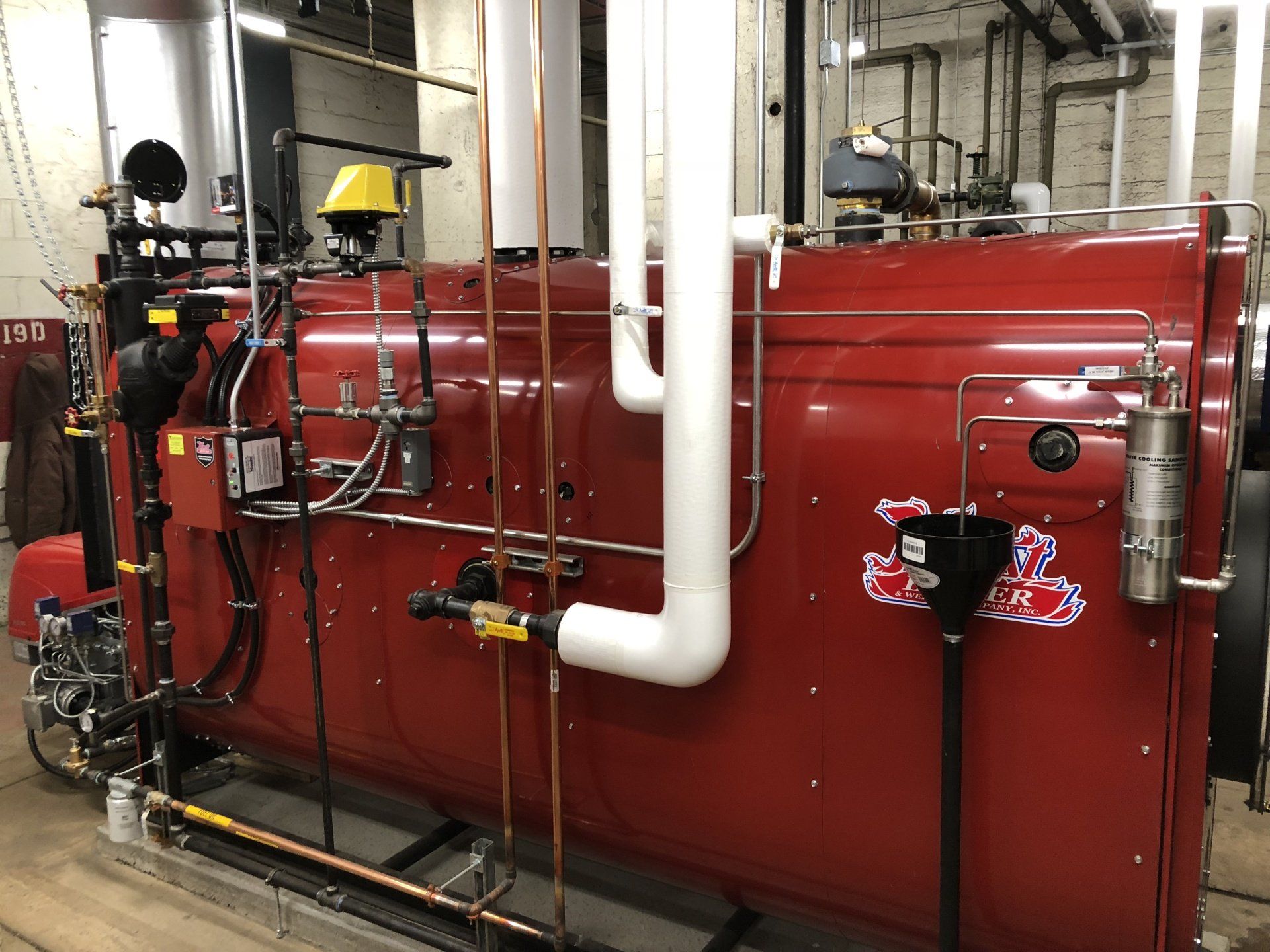 Red industrial boiler with pipes in an equipment room.