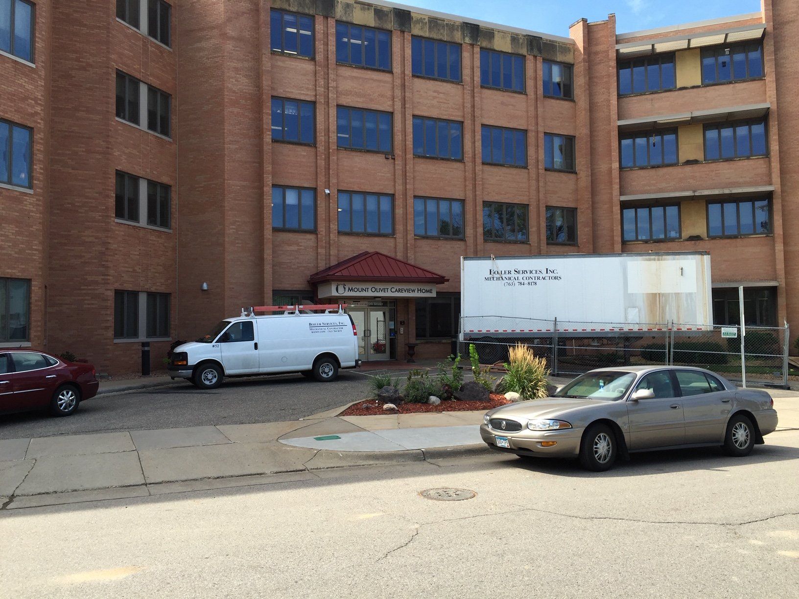 Brick building with multiple windows, white van, car, and sign out front.