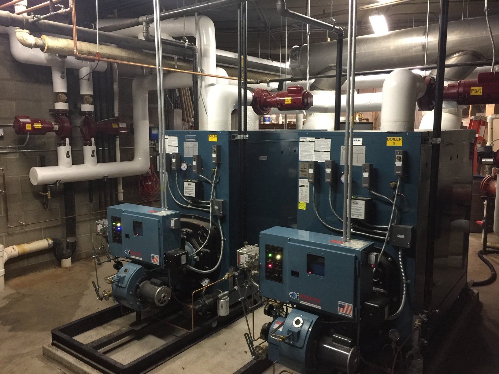 Two blue industrial boilers in a mechanical room with pipes.