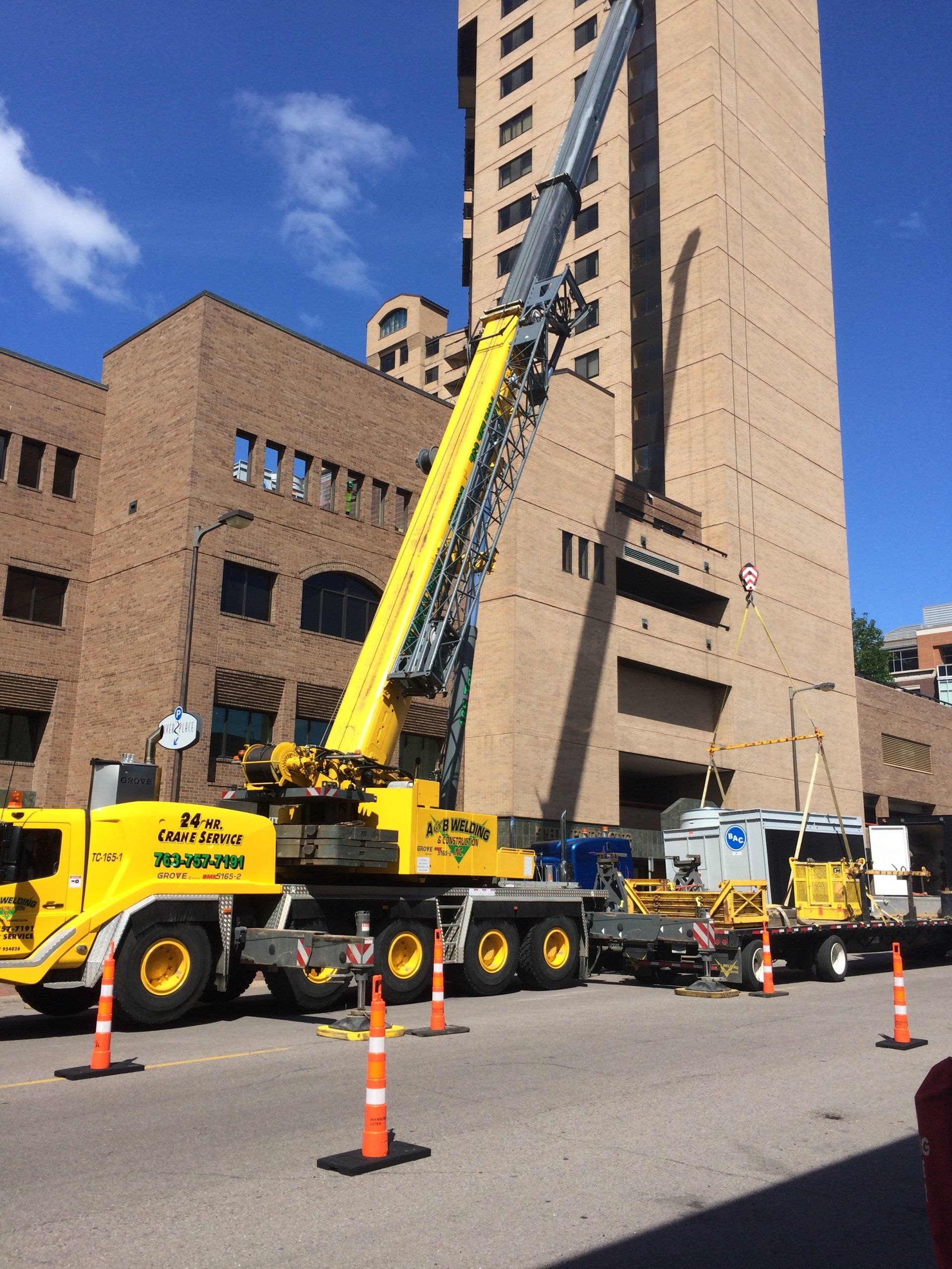 A yellow crane lifting near a tall brick building on a city street, with construction equipment nearby.