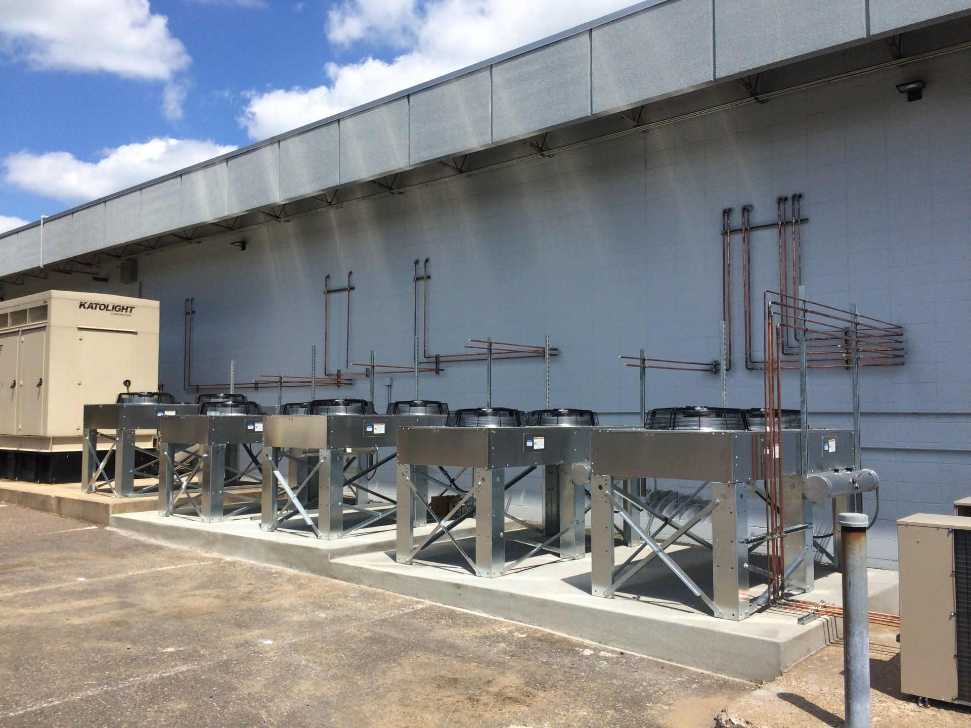 Outdoor air conditioning units mounted on a platform against a gray building wall.