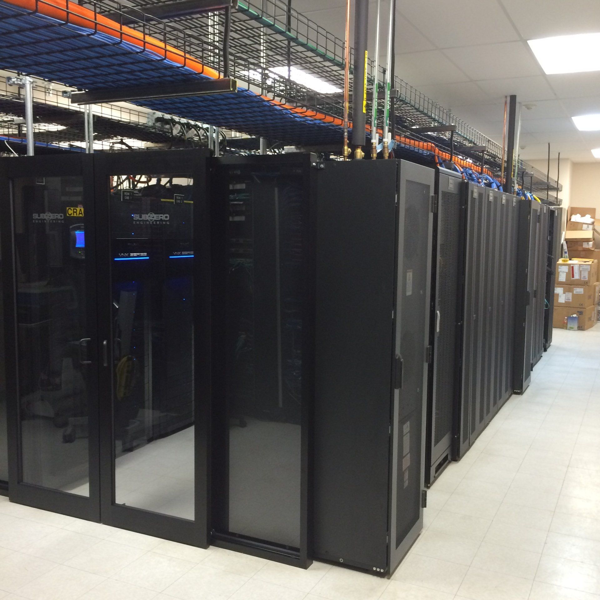 Data center with rows of black server racks, cables overhead, bright room.