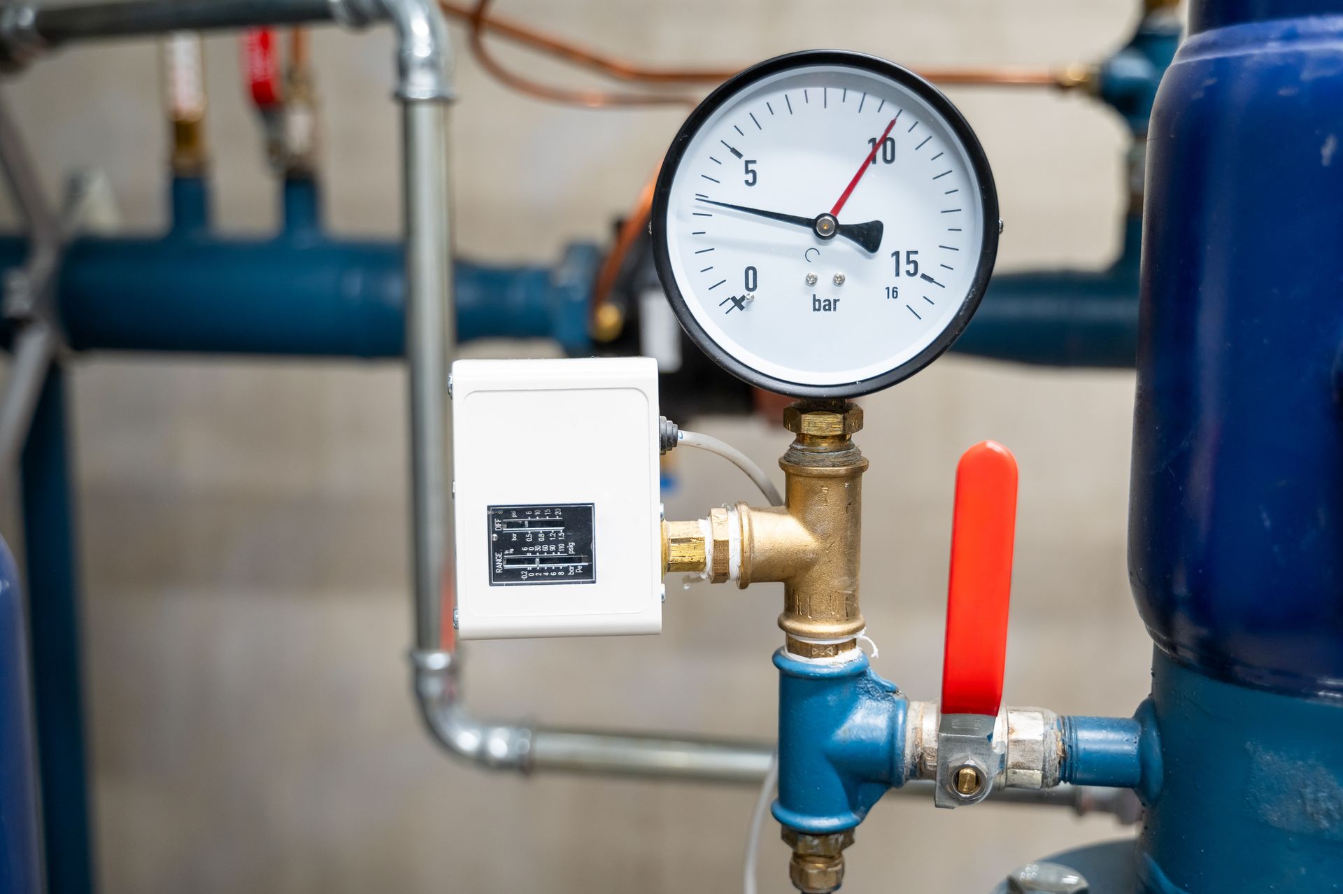 Water pressure sensor in pipes of commercial boiler room, surrounded by pipes and levers.
