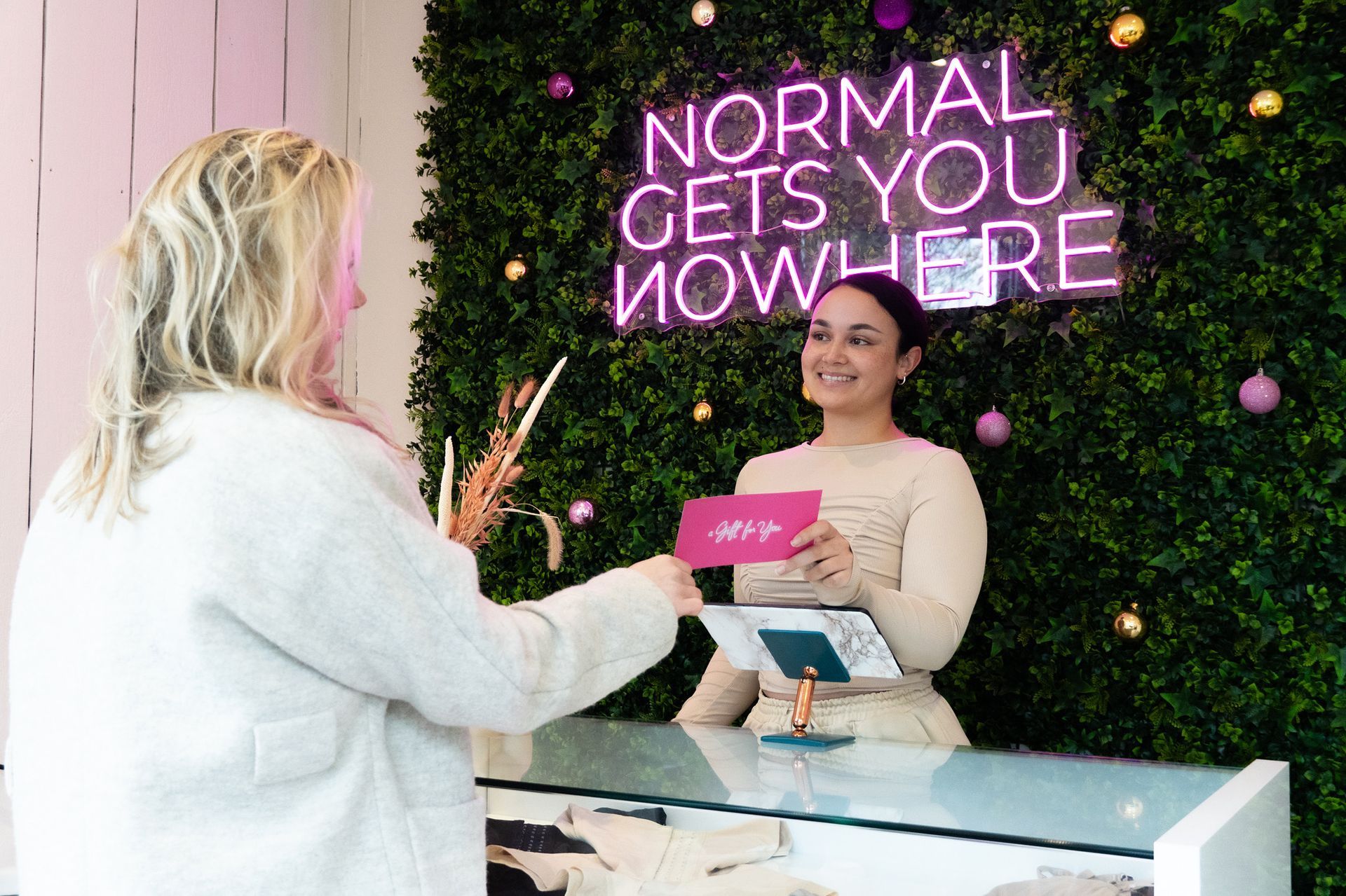 Een vrouw zit aan een toonbank in Rotterdam voor een neonbord met de tekst: ``Normaal kom je nergens''.