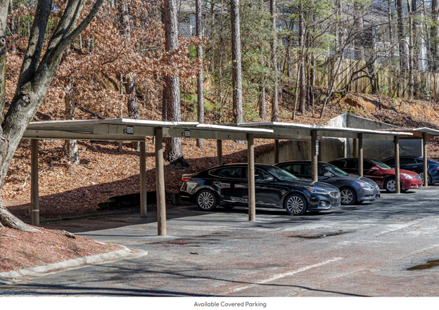 A row of cars are parked under a canopy in a parking lot.