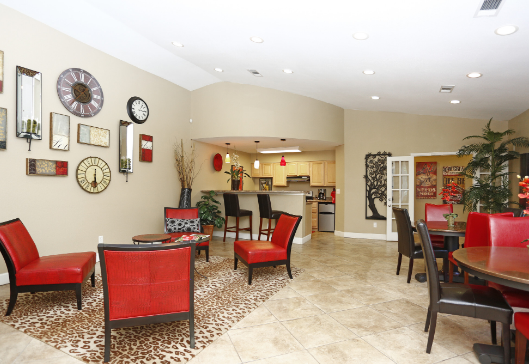 A living room with red chairs and tables and a sign on the wall that says real